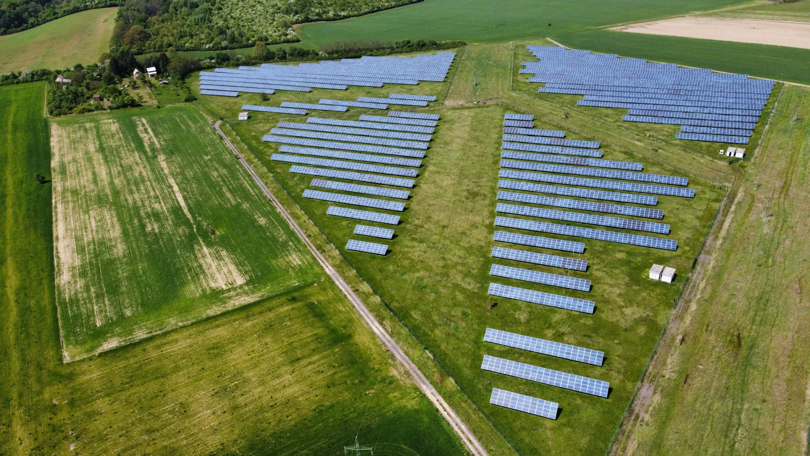 Letecký pohled na fotovoltaickou elektrárnu obklopenou zelenými poli
